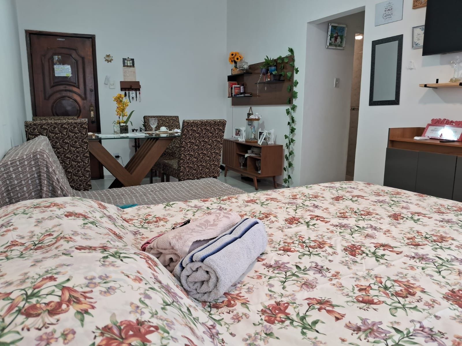 A hotel room with a bed, a dining table with chairs, a small cabinet, and a mirror on the wall.