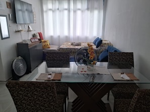 A modern living room with a glass dining table, patterned sofas, a large bed with a zebra print bedspread, and a standing fan. - Superb 1-bedroom studio in enchanting Niterói perfect for your stay (Niterói)