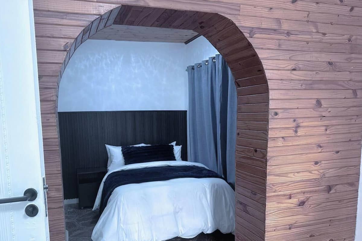 Un dormitorio con una cama, cabecera y un arco de madera.