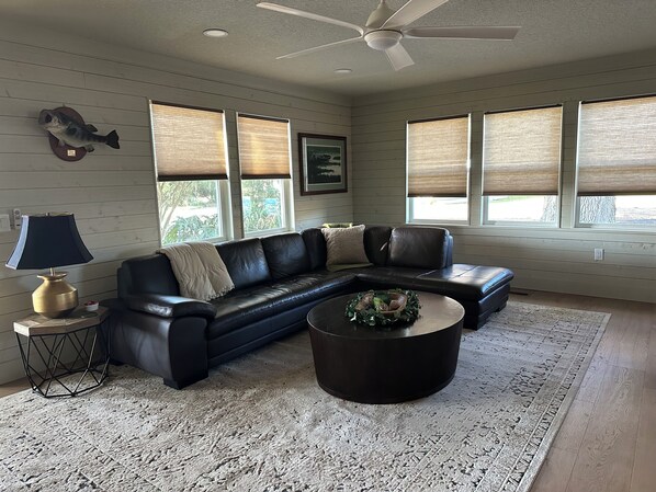 A living room with a black leather sectional sofa, a round coffee table, a lamp, and a ceiling fan.