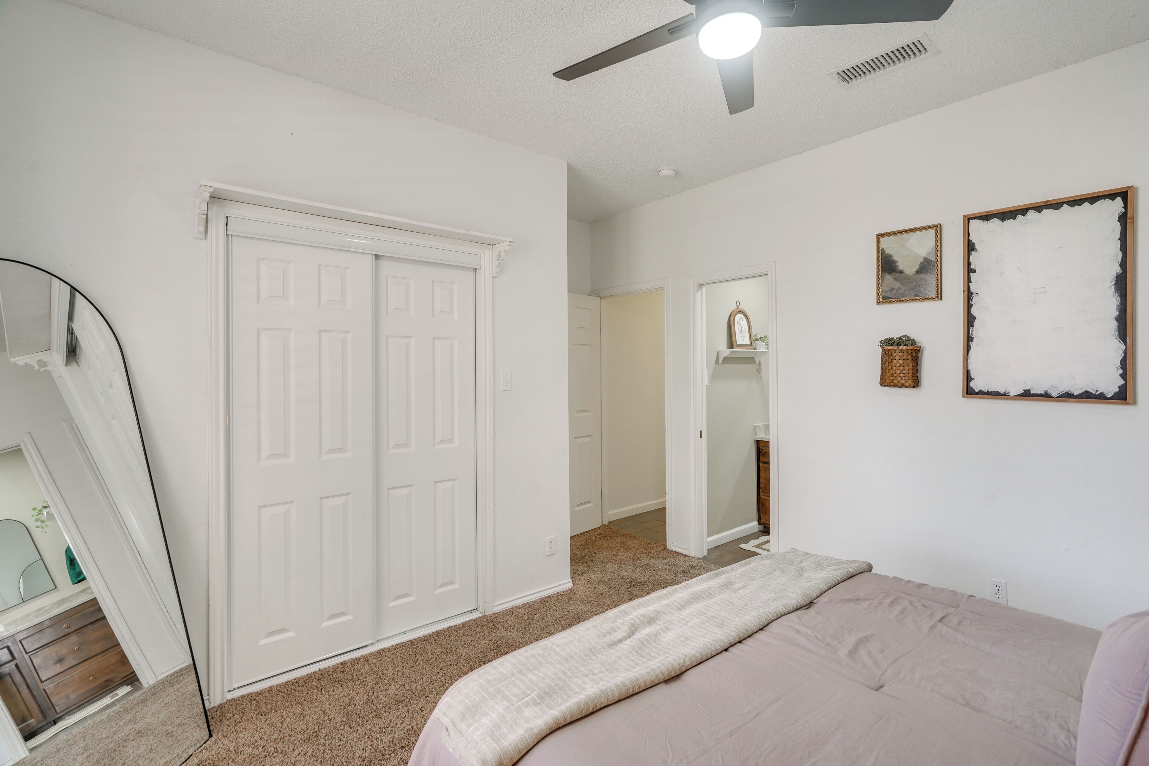 Une chambre à coucher comprenant un lit, un ventilateur de plafond, un placard et un couloir menant à une autre pièce.