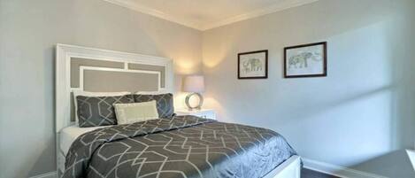 Une chambre à coucher avec un lit, une table de chevet et une lampe fixée au mur. Deux tableaux encadrés sont accrochés au mur.