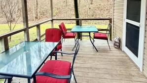 Una terrazza esterna coperta con tavolo in vetro e sedie rosse, pavimento in legno e vista su una zona boschiva.