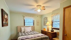 Una camera da letto con un letto, un comodino, una lampada, una ventola a soffitto e una porta.