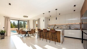 Uma cozinha moderna com revestimento de mármore, detalhes em madeira e uma área de jantar com vista para a piscina.