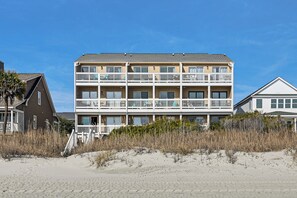 A beachfront hotel with multiple balconies, a sandy beach in front, and a clear blue sky. - Steps to Pool & Beach: Coastal Carolina Condo! (Surfside Beach)