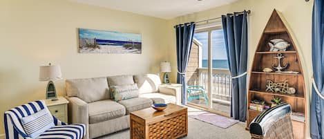 Ein Wohnzimmer mit einer Couch, einem gestreiften Sessel, einem Holztisch, einem Bücherregal und einem Bild von einer Strandlandschaft.