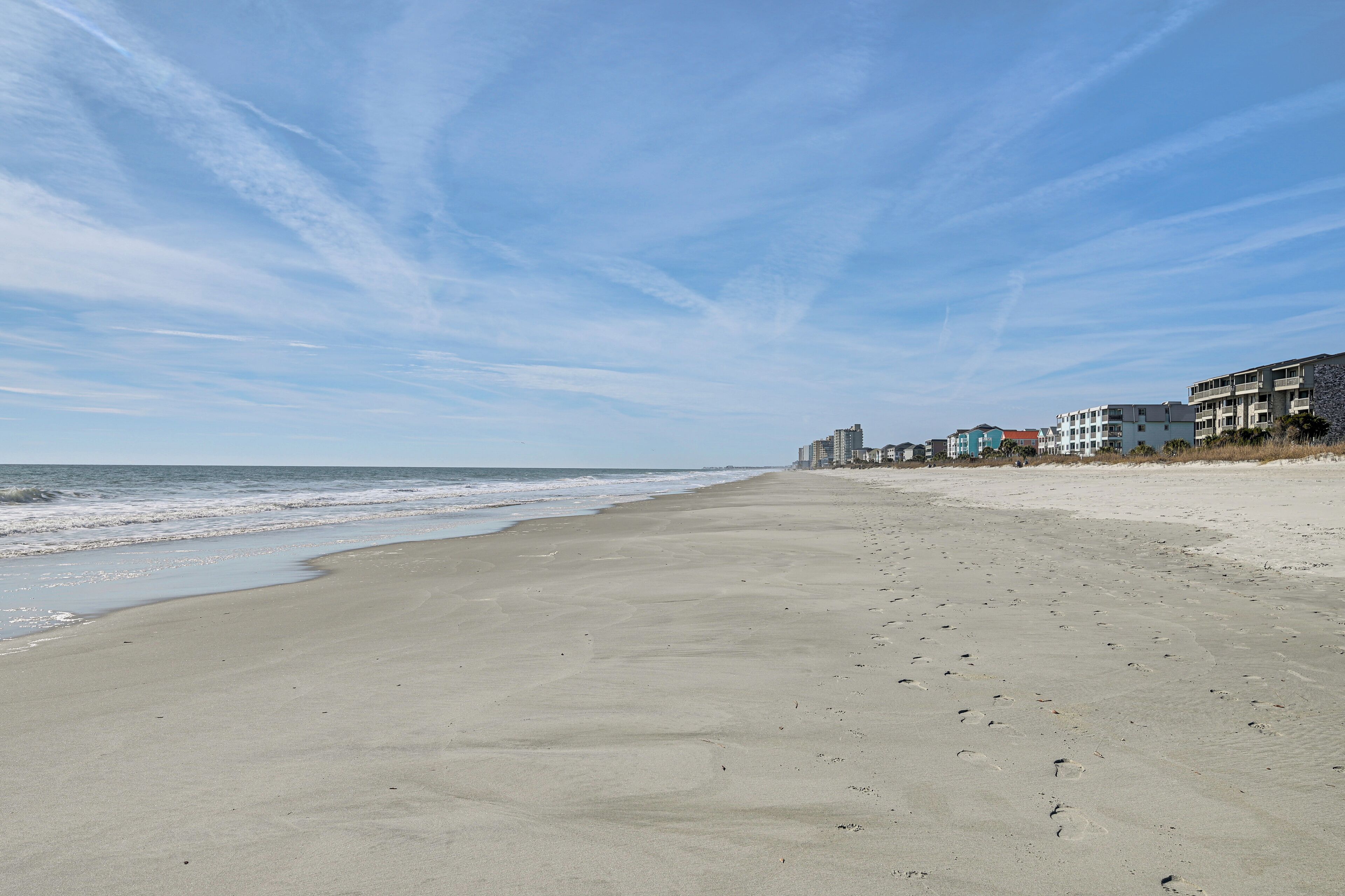 A beach with a clear sky, sandy shore, and buildings in the background.