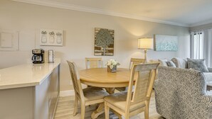 A dining area with a round wooden table and chairs, a coffee maker, and a lamp. There is a sofa with patterned cushions in the background. - 2 Mi to Tigertail Beach! Resort-Style Gem w/ Pool (Marco Island)
