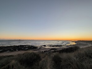 Een strand met een rotsachtige kustlijn en zandduinen begroeid met gras.