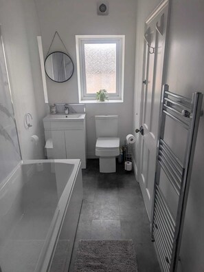 Een moderne badkamer met een bad, toilet en wastafel.