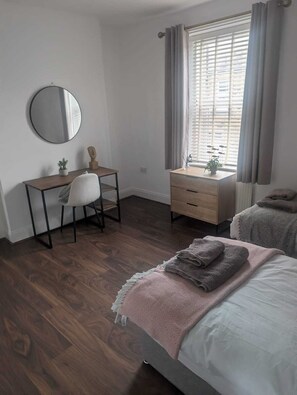 Een slaapkamer met een bed, een bureau, een stoel, een dressoir en een raam met gordijnen.