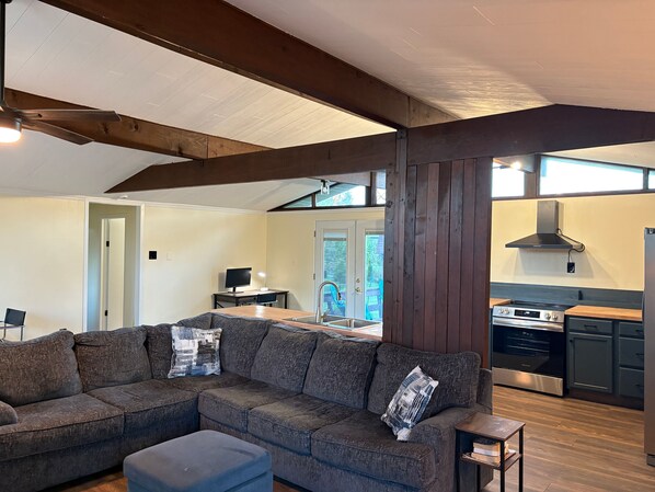 A modern living room with a sectional sofa, a small table, and a kitchen area with a stove and sink.