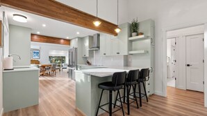 Een moderne keuken met een centraal eiland, barkrukken en een eethoek met een houten tafel en stoelen.