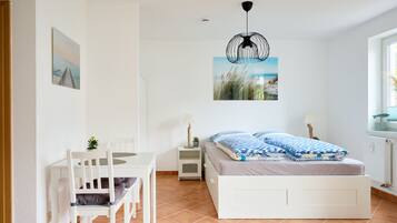 Een slaapkamer met een bed, een bureau, stoelen, een hanglamp en een raam.