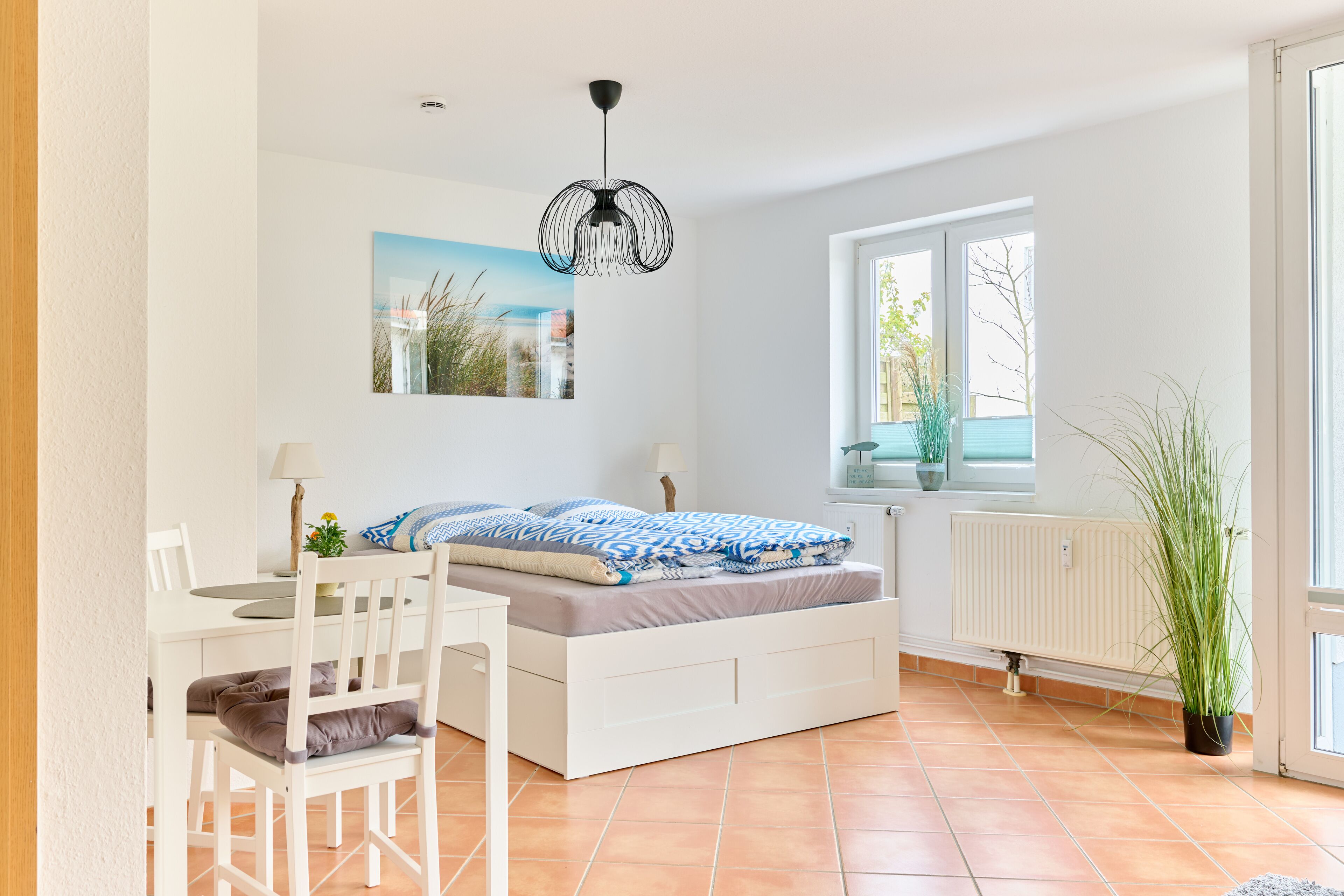 A bedroom with a bed, a desk, a chair, a radiator, and a window with a view of the outside.