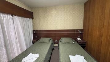 A hotel room with two single beds, a wooden headboard, a patterned wall, and a curtain.