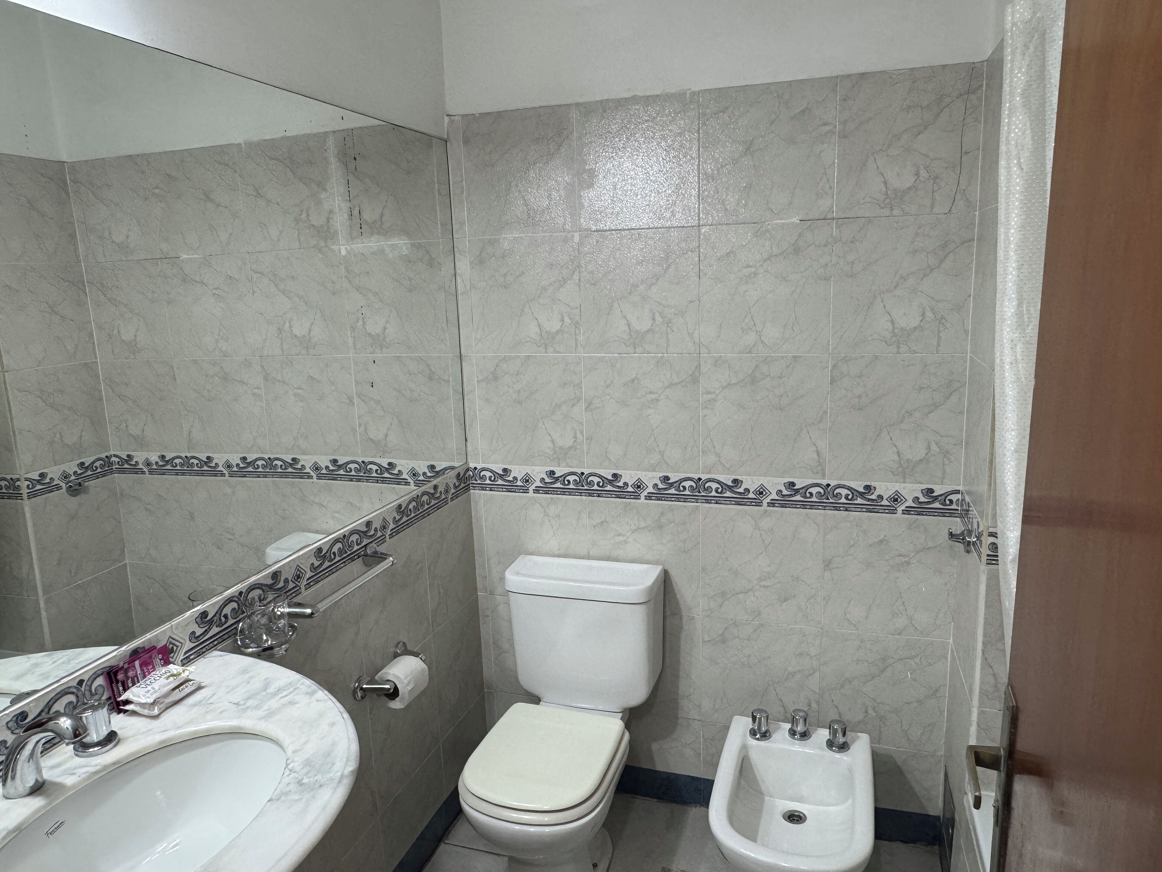 Un baño con lavamanos de mármol, inodoro, bidé y azulejos decorativos.