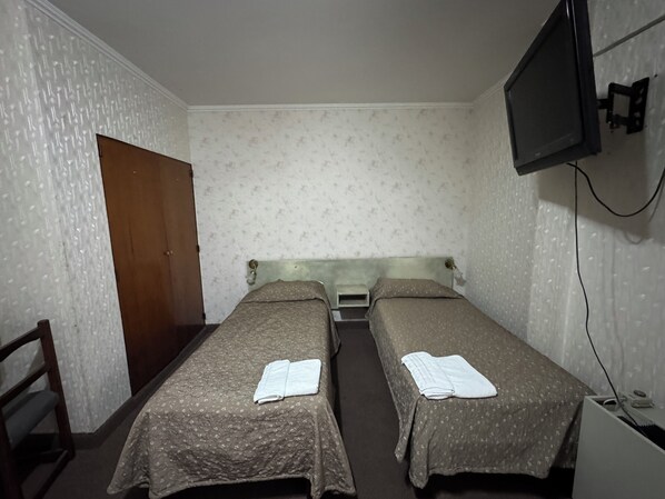 A room with two single beds, a wooden chair, a television mounted on the wall, and a door.