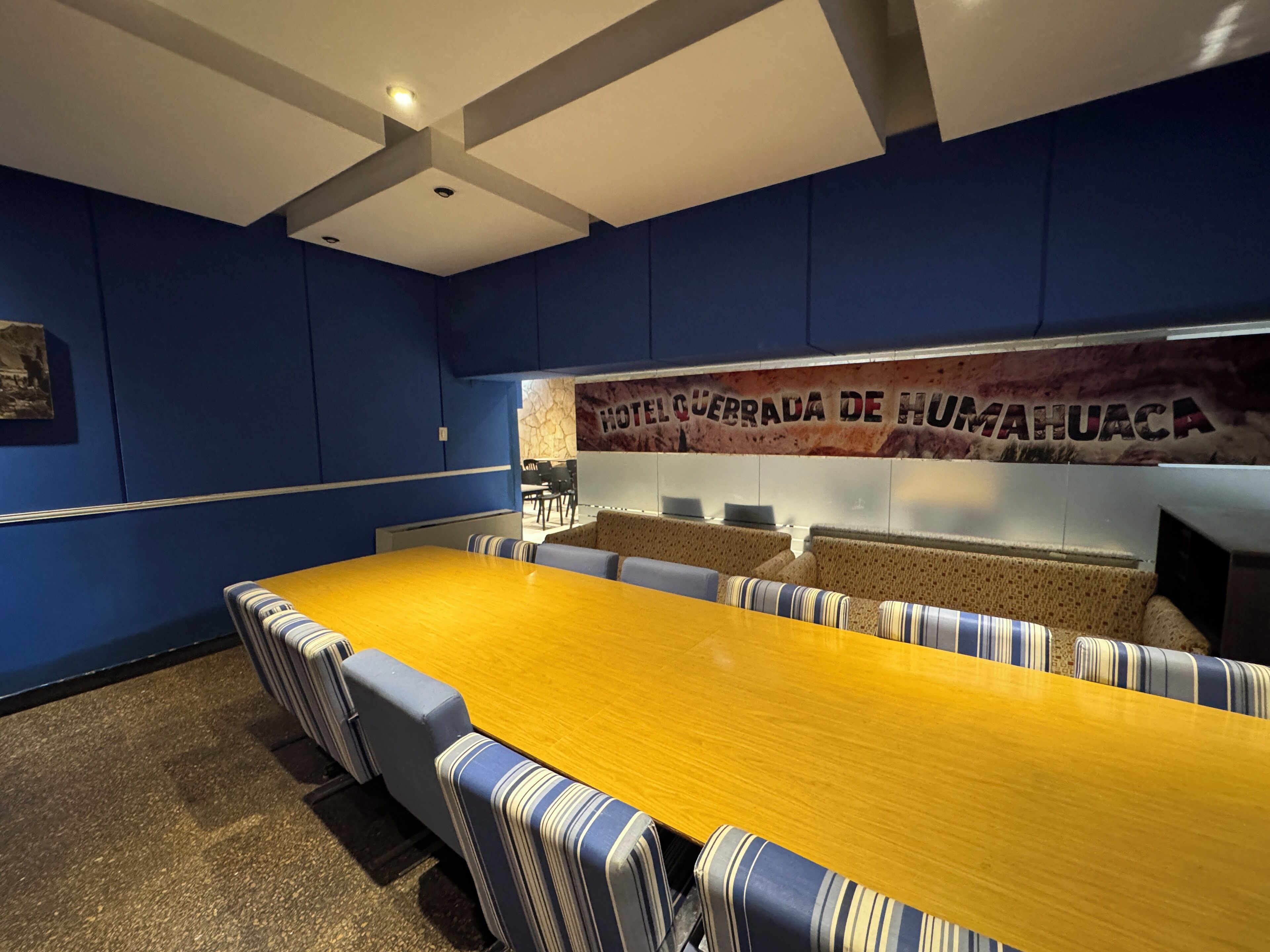A conference room with a long table, striped cushioned benches, and a banner reading "HOTEL CERRADA DE HUMAUACA".