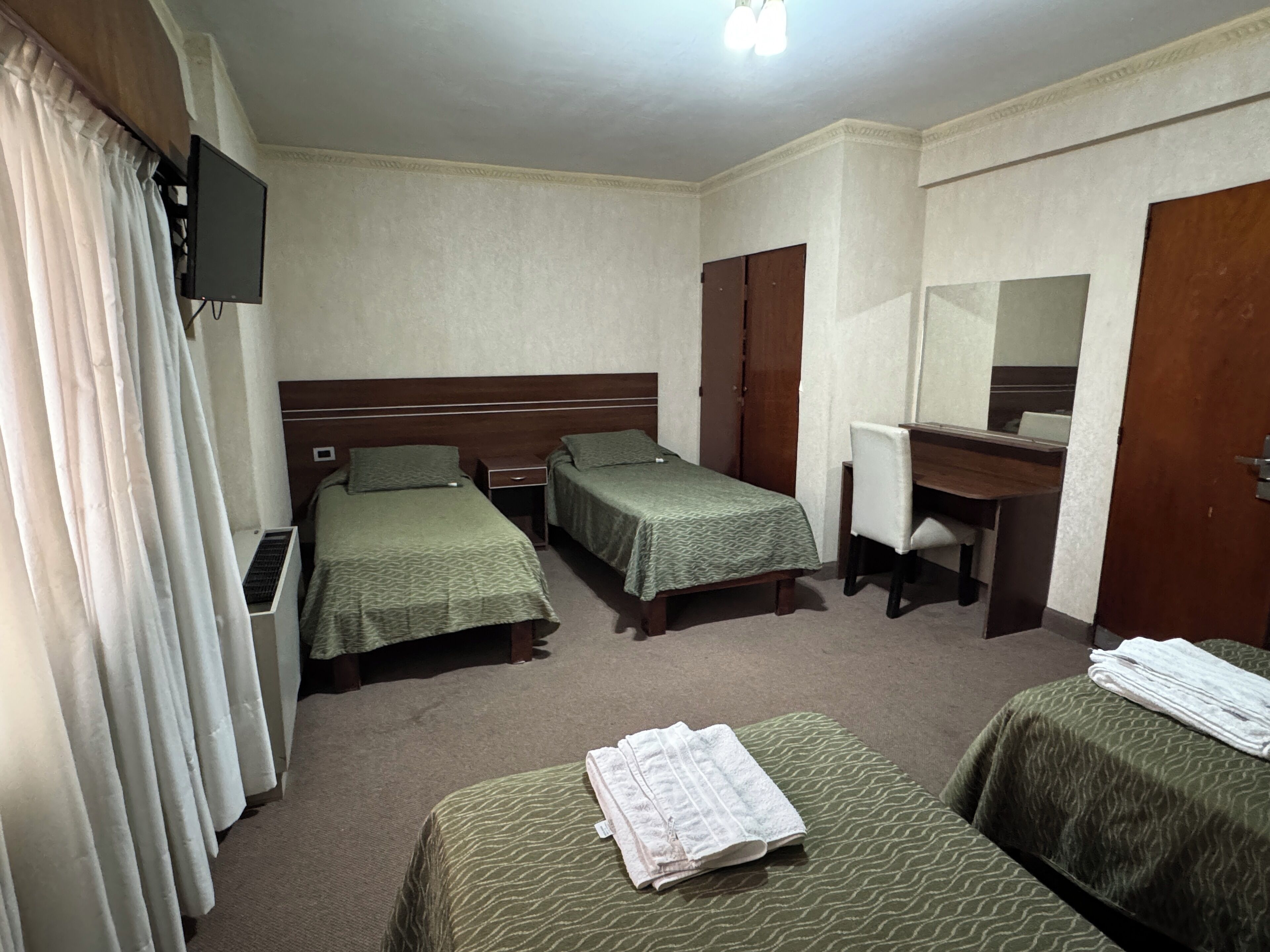 A hotel room with two single beds, a desk with a chair, a mirror, and a television on the wall.