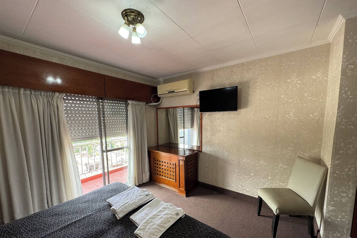 Ein Hotelzimmer mit Bett, Schreibtisch, Stuhl, Fernseher und einem Balkon mit Vorhängen.