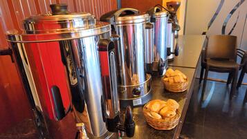 A coffee station with several stainless steel coffee dispensers and baskets of bread.