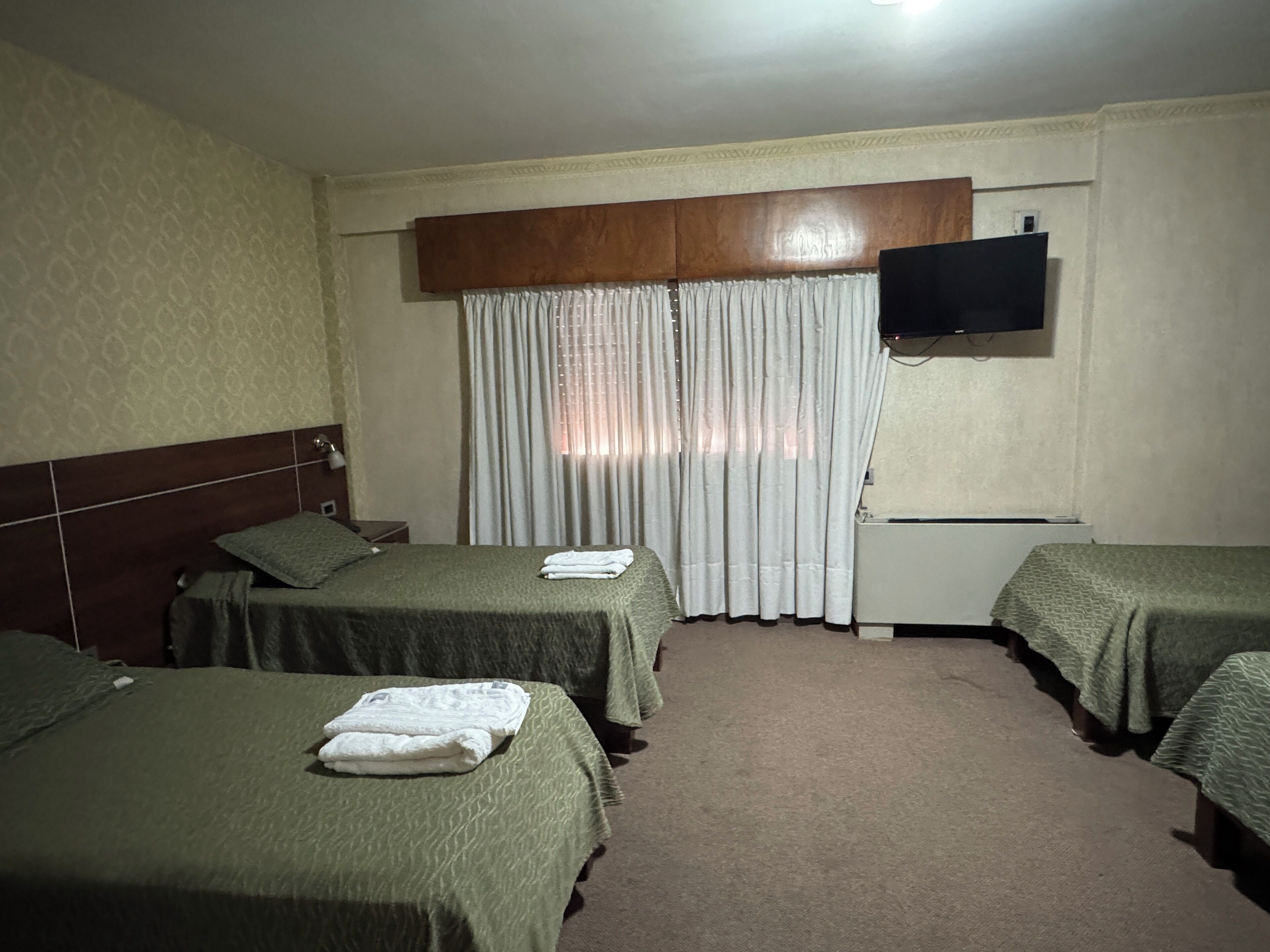 Habitación de hotel con dos camas individuales, un televisor montado en la pared y una ventana con cortinas.