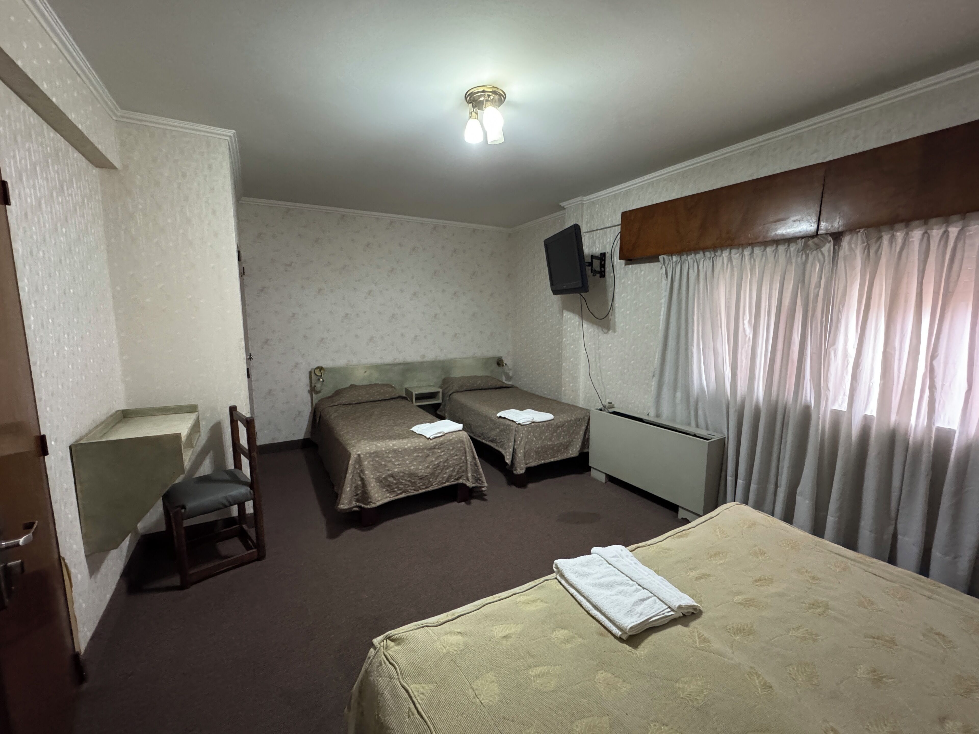 A hotel room with two single beds, a TV mounted on the wall, a small table, and a chair.