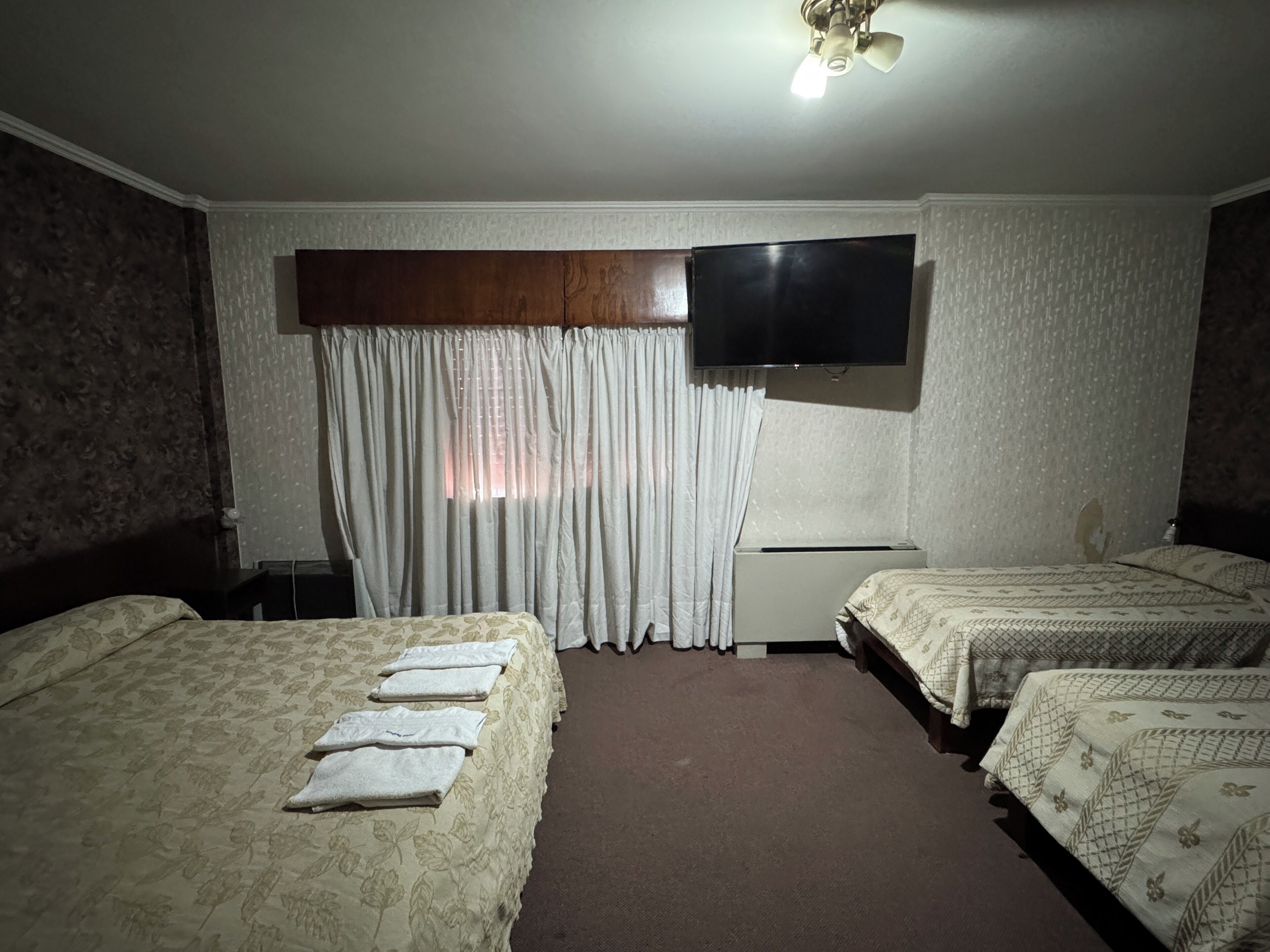 A hotel room with two beds, a flat-screen TV mounted on the wall, a desk, and a ceiling fan.