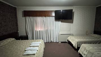 A hotel room with two beds, a flat-screen TV mounted on the wall, a desk, and a ceiling fan.
