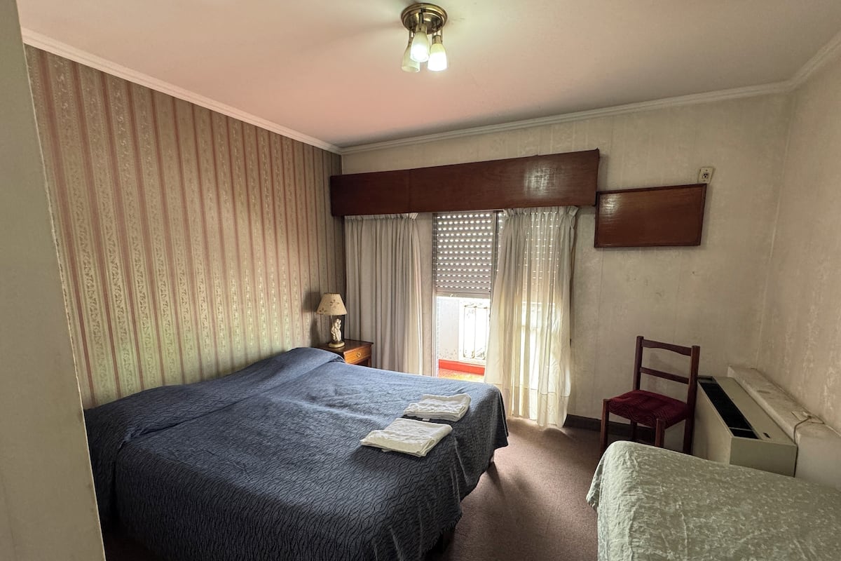 Ein Hotelzimmer mit einem großen Bett, einem Sessel, einem Schreibtisch und einem Fenster mit Vorhängen.