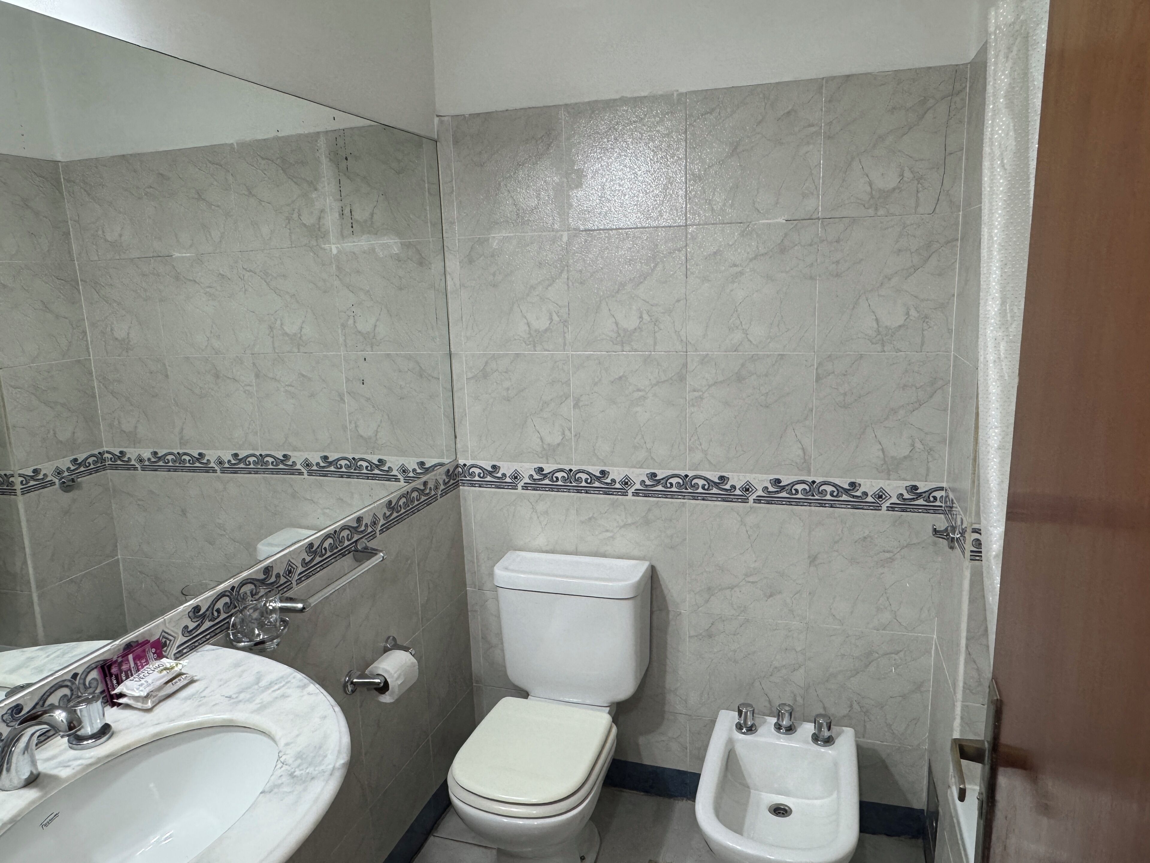 A bathroom with a marble sink, toilet, bidet, and decorative tile border.