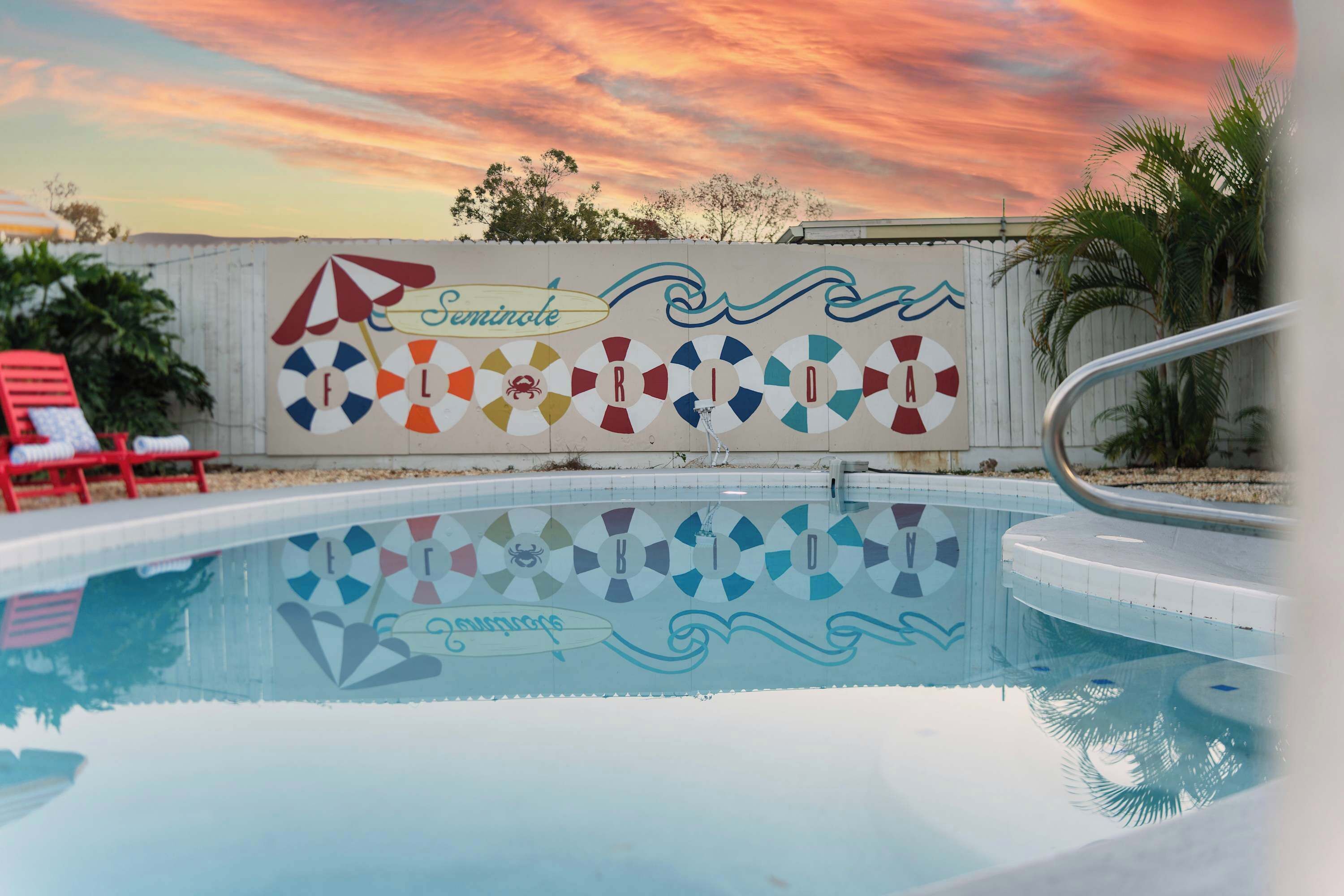 A swimming pool with a lifeguard mural and a sunset in the background.