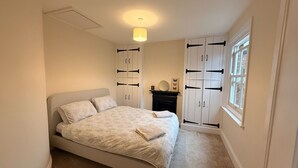 A bedroom with a bed, a wardrobe, a fireplace, and a window. - Snug cottage in the South Downs (Walderton)