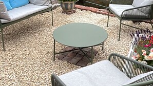 A patio area with a round table and four chairs, surrounded by pebbles and greenery. - Snug cottage in the South Downs (Walderton)