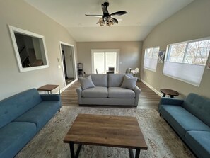 Ein geräumiges Wohnzimmer mit grauem Sofa, einem Holztisch und einem Deckenventilator.