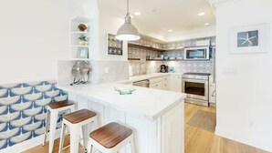 A modern kitchen with white cabinetry, a central island, and a microwave. - Oceanfront Escape | Steps to Beach | Sleeps 7 (Carlsbad)