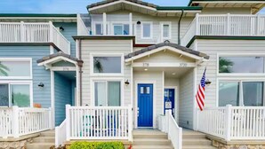 A two-story house with a blue front door, white railings, and an American flag. - Oceanfront Escape | Steps to Beach | Sleeps 7 (Carlsbad)