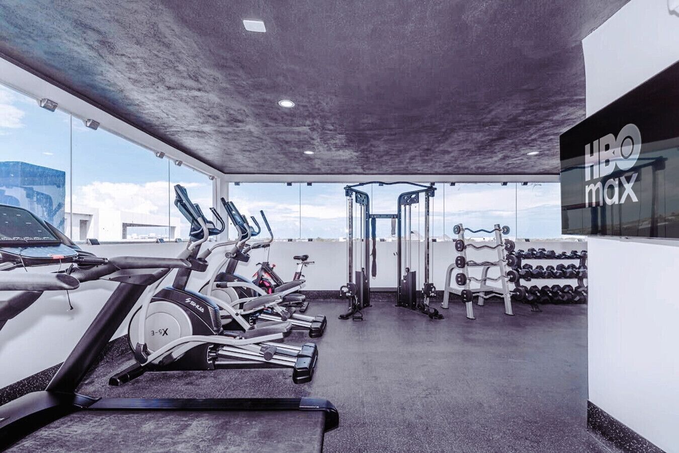 Une salle de sport équipée de machines de cardio, de bancs de musculation et d’un porte-haltères fixé au mur.