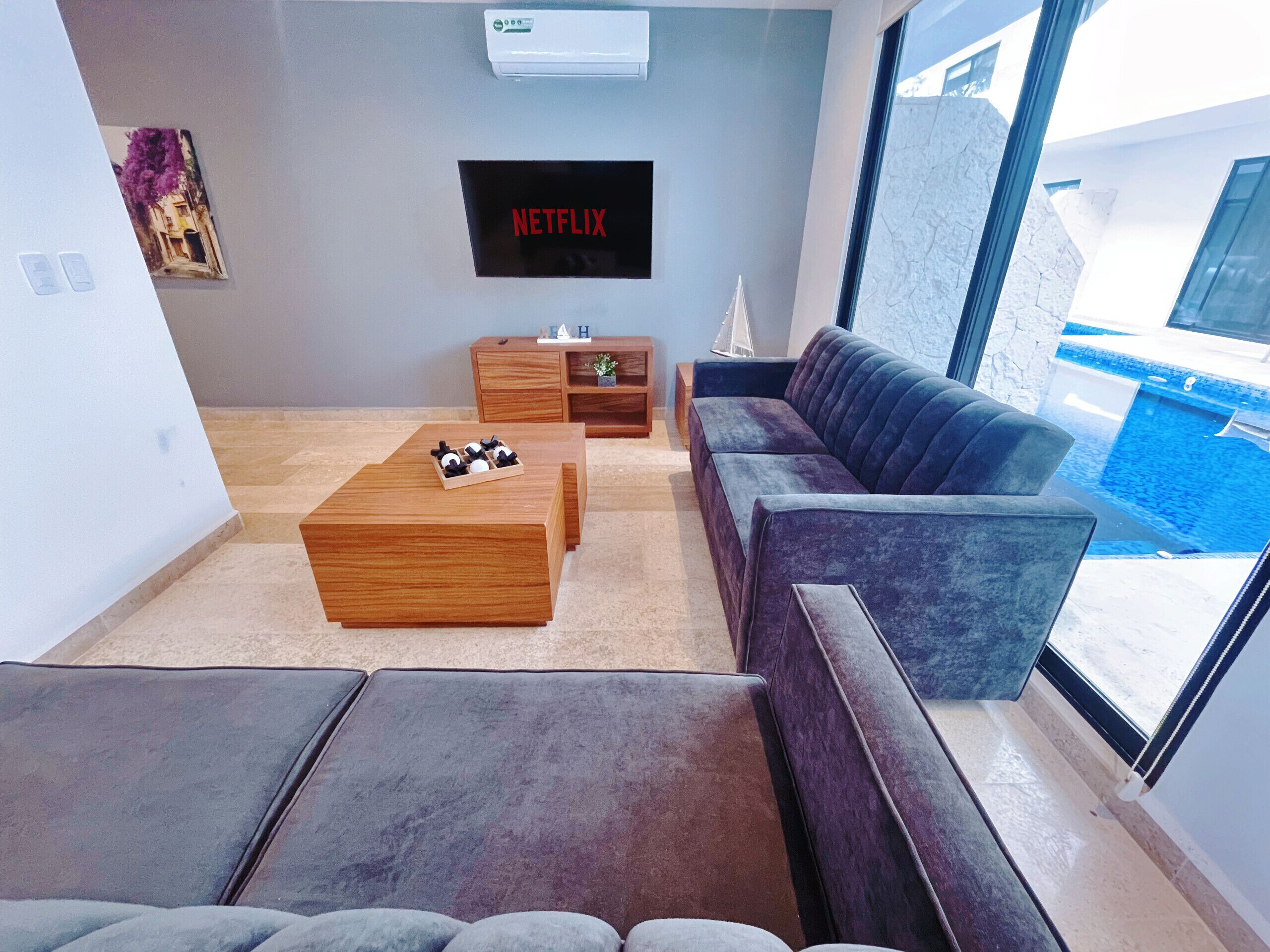 Ein modernes Wohnzimmer mit Couchtisch aus Holz, grauem Sofa und Wandfernseher, der 'NETFLIX' zeigt.