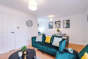 A modern living room with a green sofa, a coffee table, and a dining area with a small table and chairs. - Modern 1BR MediaCity Stay - Free Parking - M50 (Manchester)