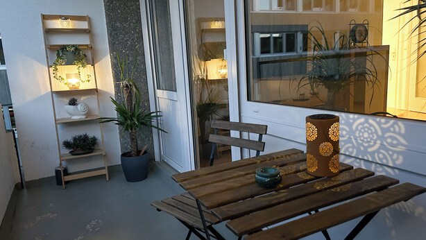 A small patio area with a wooden table, benches, and potted plants. - Cozy bright apartment centrally located with balcony and parking space (Bayreuth)