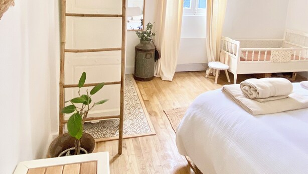 Une piÚce lumineuse et bien éclairée, avec une échelle en bois, un berceau, une petite table et une plante en pot.