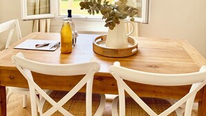 Une table Ă manger avec des chaises blanches, une table en bois, une bouteille, un menu et un vase avec une plante.