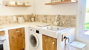 Une cuisine compacte Ă©quipĂ©e dâun lave-linge, dâun Ă©vier, de meubles en bois et dâune fenĂȘtre.