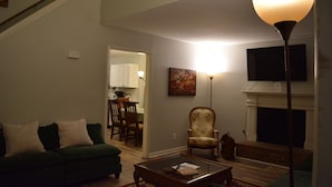 Un salon avec un canapé vert, une table basse, une cheminée et un téléviseur fixé au mur.