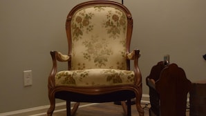 Une chaise recouverte d’un tissu à motifs floraux, une lampe et un tableau accroché au mur.