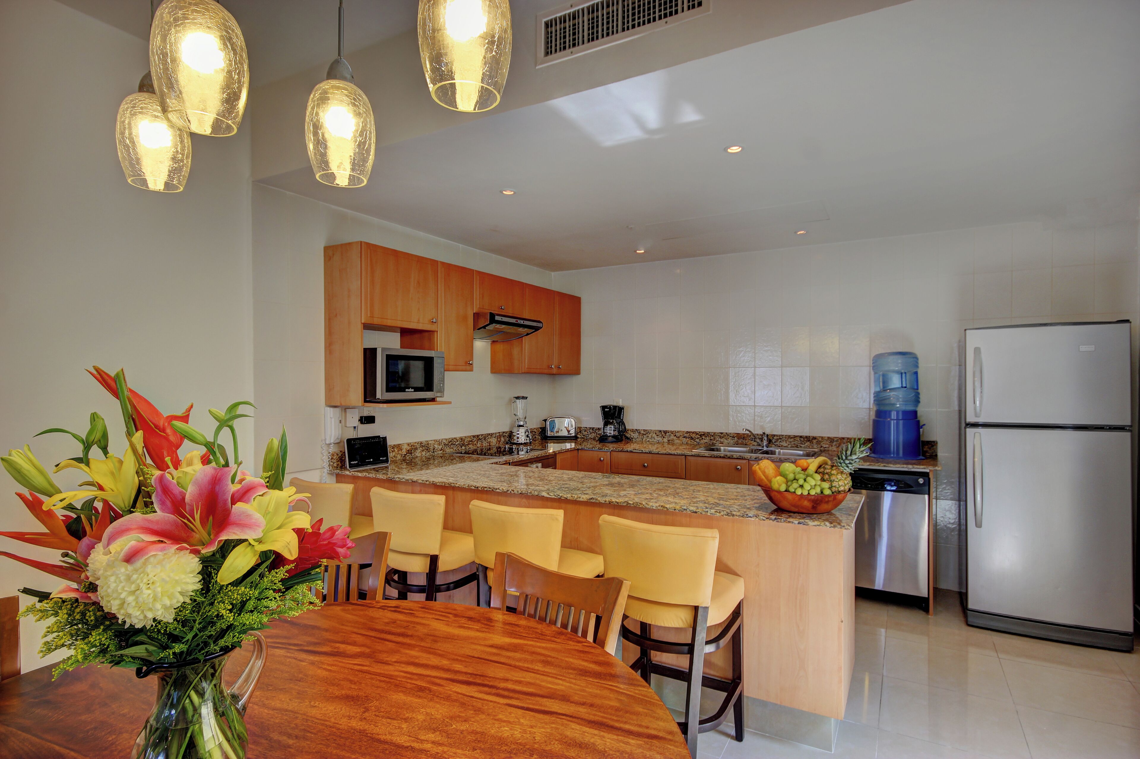 A modern kitchen with granite countertops, wooden cabinets, a stainless steel refrigerator, and a dining area with a wooden table and chairs.