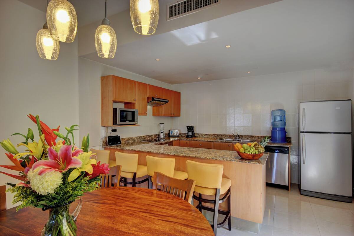 A modern kitchen with a central island, wooden cabinets, stainless steel appliances, and a dining area with a wooden table and chairs.